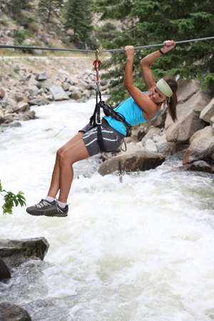 An attractice and atletic girl makes tyrolean traverse over a rushing riverの写真素材