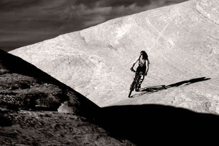 A biker descending into the shadows on a trail near Moab, Utah.の写真素材