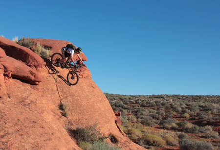 A rider drops down a steep sandstone feature in the Utah desert.の写真素材