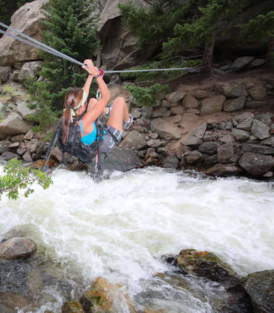 A woman crosses a raging creek via a risky tyrolean traverse.の写真素材