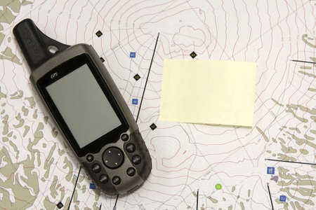 A hand held GPS device sits on a topo map.  The blank screen and a blank yellow sticky note are ready for your text.の写真素材