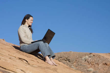 A beautiful woman displays the miracle of wireless connectivity and laptop computers as she surfs the web in the middle of the desert.の写真素材