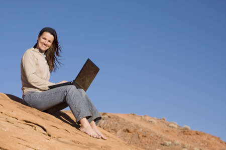 A beautiful woman displays the miracle of wireless connectivity and laptop computers as she surfs the web in the middle of the desert.の写真素材
