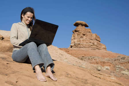 A beautiful woman displays the miracle of wireless connectivity and laptop computers as she surfs the web in the middle of the desert.の写真素材