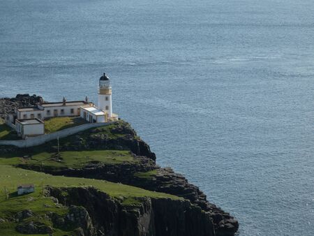 Lighthouse with yellow details on top of a green cliff