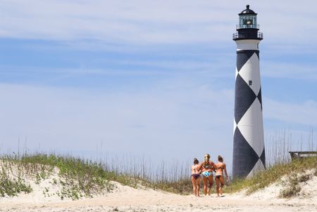 Three sunbathers walking towards a historic lighthouse.の写真素材
