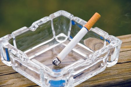 A cigarette burning in a glass ashtray.の写真素材