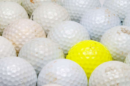 A yellow golf ball in the middle of white balls.の写真素材