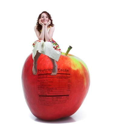 A beautiful young woman sitting on a whole red delicious apple with a nutrition labelの写真素材