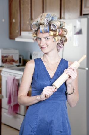 A beautiful young woman housewife with curlers in her hair holding a rolling pinの写真素材