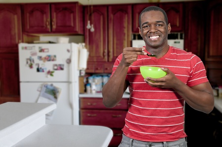 Young black African American man eating food from a bowl in a home kitchenの写真素材