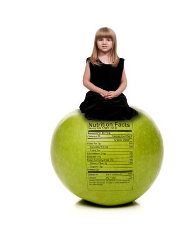 Beautiful little girl sitting on aGranny Smith green apple with a nutrition labelの写真素材