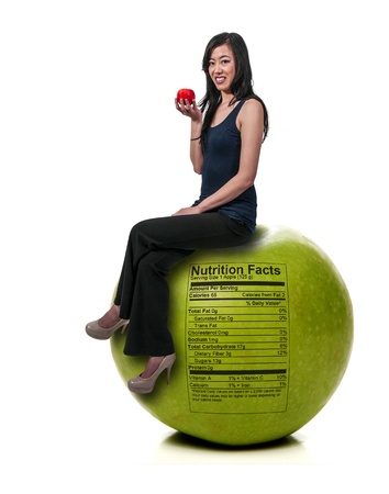 Beautiful young Asian woman sitting on a whole red delicious apple with a nutrition labelの写真素材