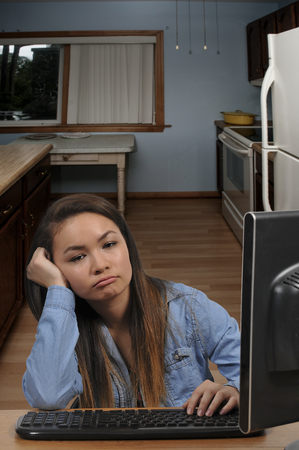 Frustrated bored teenage girl using a desktop computer to do homeworkの写真素材