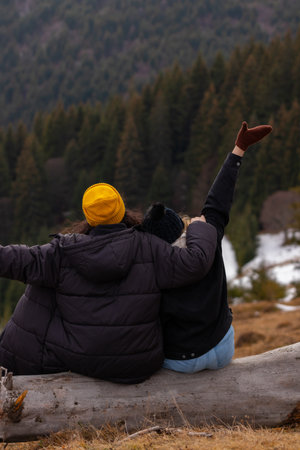 Two girls sitting on a log. Friendship and adventure on the mountainの写真素材