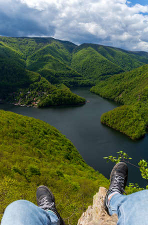 View from the mountain. A person sitting on a rock and looking at the lake and the mountains in front of him. Tarnita Lake located between the mountains, Cluj, Romania photographed from Lucaci's stoneの写真素材