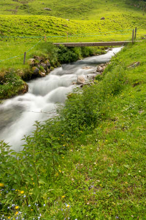 Appenzell, Switzerland, June 13, 2021 Small river flows down the mountains along a green fieldの写真素材