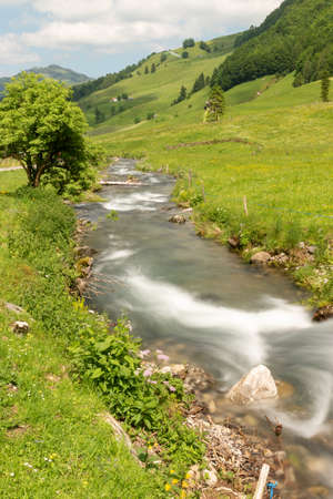 Appenzell, Switzerland, June 13, 2021 Small river flows down the mountains along a green fieldの写真素材