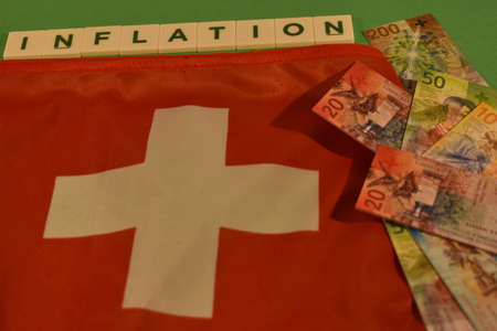 Vaduz, Liechtenstein, November 22, 2021 Switzerland national flag with some toy money and the word inflationの写真素材
