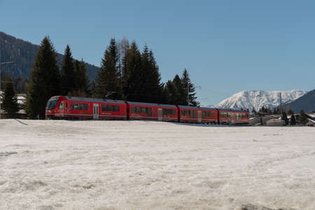 Davos, Switzerland, March 23, 2022 Local train is passing a snow covered winter landscape on its way...