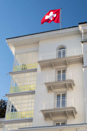 Davos, Switzerland, March 23, 2022 Waving swiss national flag on the roof top of the hotel Belvedere in the city center on a sunny dayのeditorial素材