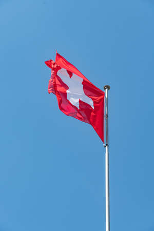 Truebbach, Switzerland, April 28, 2022 Swiss national flag is waving in the wind on the rhine bridge...