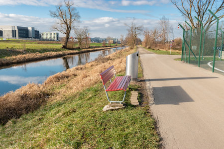 Zurich, Switzerland, January 19, 2023 A red empty bench next to a small river on a sunny day just at the international airportのeditorial素材