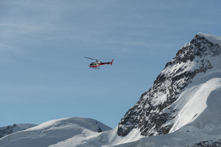 Jungfraujoch, Canton Bern, Switzerland, February 11, 2023 Helicopter is flying along the snow covered mountains on a sunny dayのeditorial素材