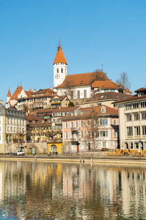 Thun, Switzerland, February 13, 2023 Waterfront at the Aare river in the city center with the historic city church on a hill in the backgroundのeditorial素材