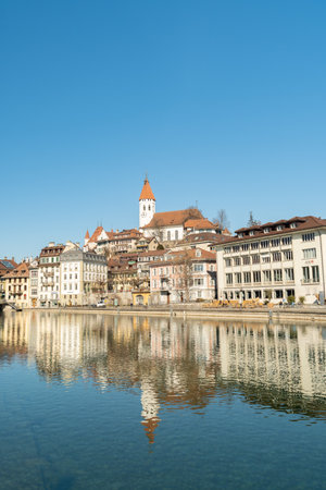 Thun, Switzerland, February 13, 2023 Waterfront at the Aare river in the city center with the historic city church on a hill in the backgroundのeditorial素材