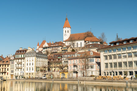 Thun, Switzerland, February 13, 2023 Waterfront at the Aare river in the city center with the historic city church on a hill in the backgroundのeditorial素材
