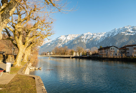 Interlaken, Switzerland, February 10, 2023 Water promenade along the Aare river in the city center with the majestic alps in the backgroundの写真素材