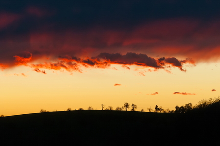 Silhouette of hilltop with orange sky and reddish clouds in the backgroundの写真素材