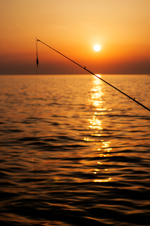 Fishing pole with sun setting over sea in the backgroundの写真素材
