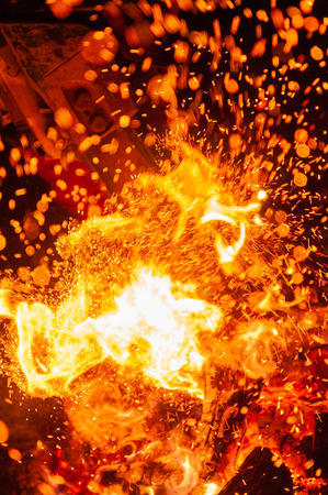 Closeup of explosive scene with chainsaw cutting through burning wood in the dark and sparks flying...