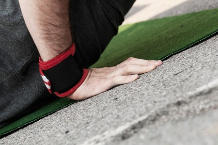 Closeup side view of a mans right hand with wrist band doing push ups on green matの写真素材
