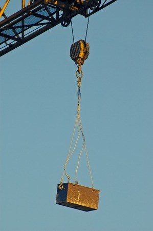 Rusty toolbox hanging off a construction crane attached by steel ceble and hook