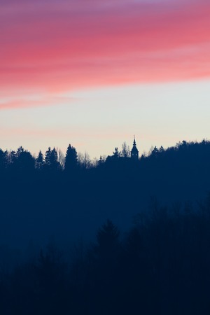 Silhouette of treetops and catholic church on a beautiful pink and bluish evening sky background. Beauty in nature and religion concepts.の写真素材