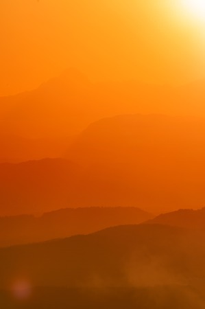 Layers of hills and mountain ranges in beautiful orange radiant light of setting sun in Slovenian...