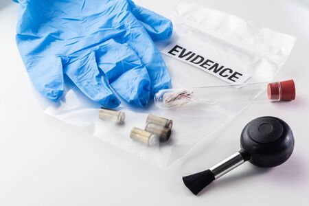 Closeup of 9 mm bullet cases in evidence bag, fibers in glass tube, blower brush and blue glove....