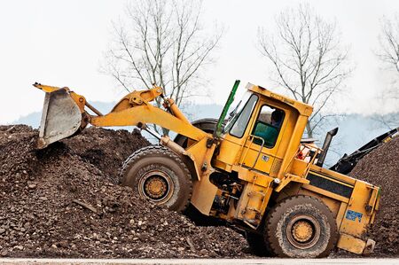 Yellow heavy wheel loader making dirt and rock piles at separation site. Heavy machinery, quarry,...