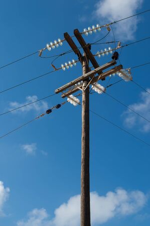 Old wooden three-phase electric utility pole with cables on a blue sky in background