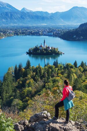 Young woman hiker with backpack enjoying the view of alpine lake Bled and mountains in background. Slovenia, Europe. Landmarks, travel, tourism and beauty of nature concepts.の写真素材