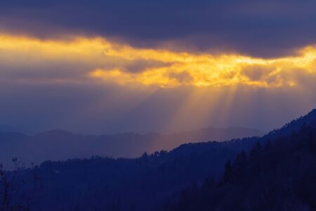 Rays of sunlight shining through clouds over dark landscape in the evening. Faith, religion, hope...