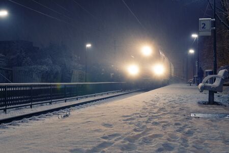 Freight train with strong headlights arriving at station on a snowy night. Travel, transportation...
