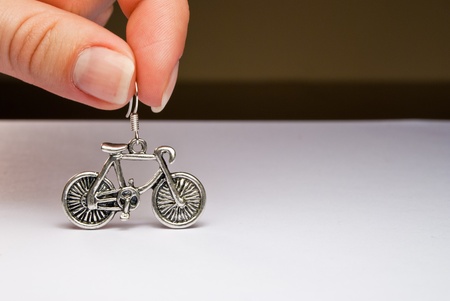 Two fingers holding a silver bicycle earringの写真素材
