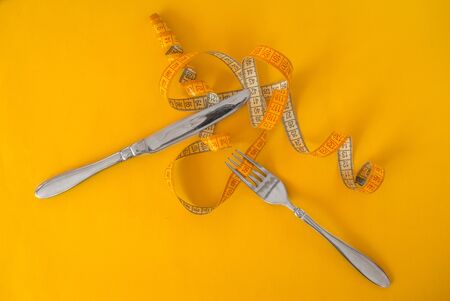 fork and knife wrapped in a meter to measure body volume on a yellow background. Diet. Proper...
