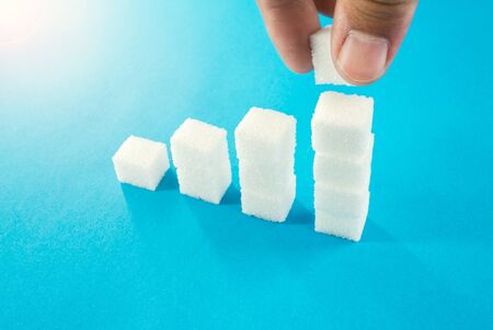 degree of sugar cubes on a blue background man's hand makes a cube. diabetes mellitus.の写真素材