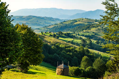 Stack of hay on a green lawn in the mountains in the morning under a blue summer sky. summer landscape of a rural valley.の写真素材
