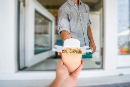 street hedgehog. A man's hand reaches for noodles in a food truck. Close-up shot of a food truck salesman serving glaps to a male customer.の写真素材